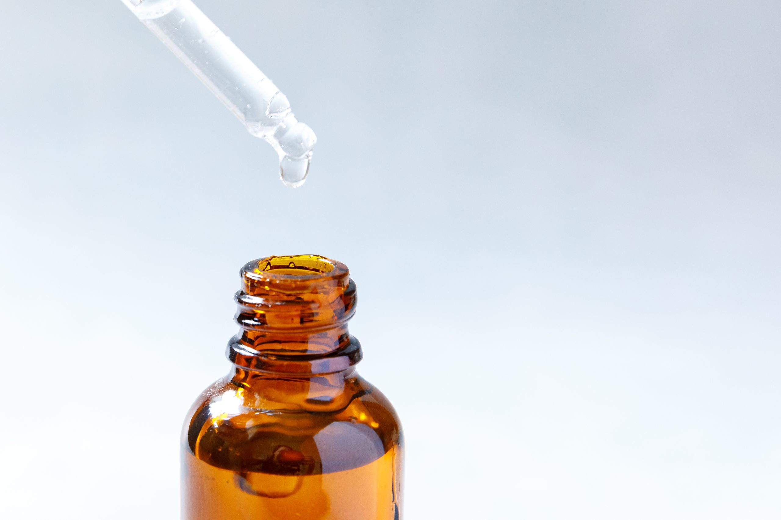 Essential oil dropping from pipette to bottle. Essence liquid cosmetic. Dropper glass bottle with liquid cosmetic serum. Syrup, perfume, aromatherapy concept. Beauty Treatment